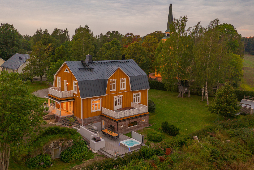 Oranssi puuhuvila Villa Degerby pihapiireineen kesällä, terassille ulkoporeallas ja pitkä pöytä - Venuu.fi